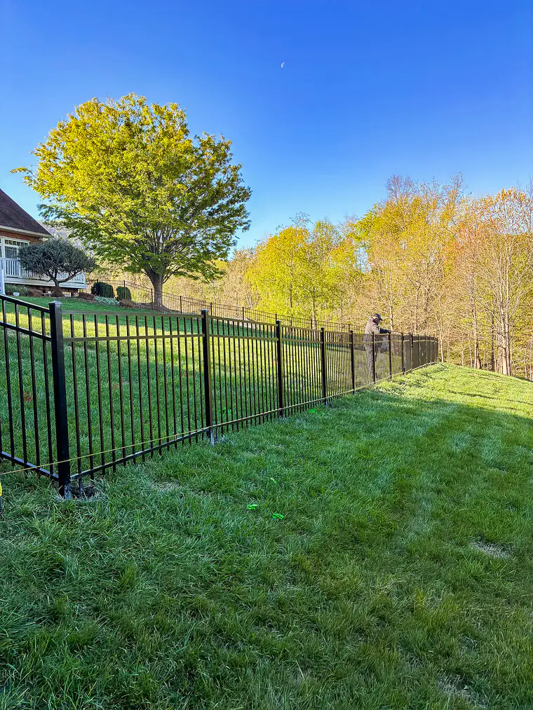 Black aluminum fence stepping down a sloped lawn with spring foliage in Roanoke