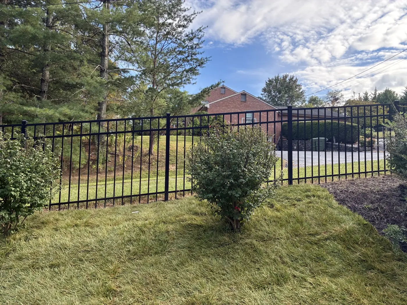 Black aluminum fence beside a brick home in autumn