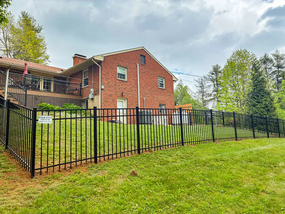 Black aluminum fence enclosing the back lawn of a brick home in Roanoke