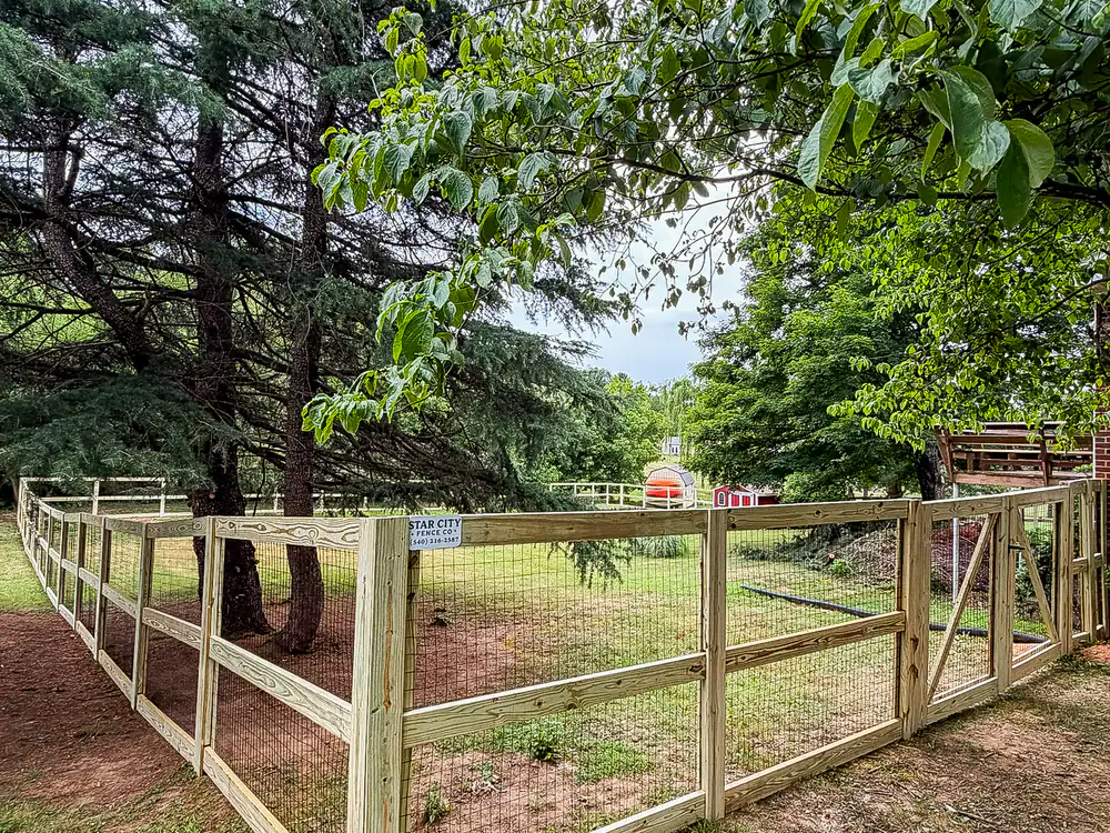 Three-rail ranch rail wood fence with wire mesh installed on a large property
