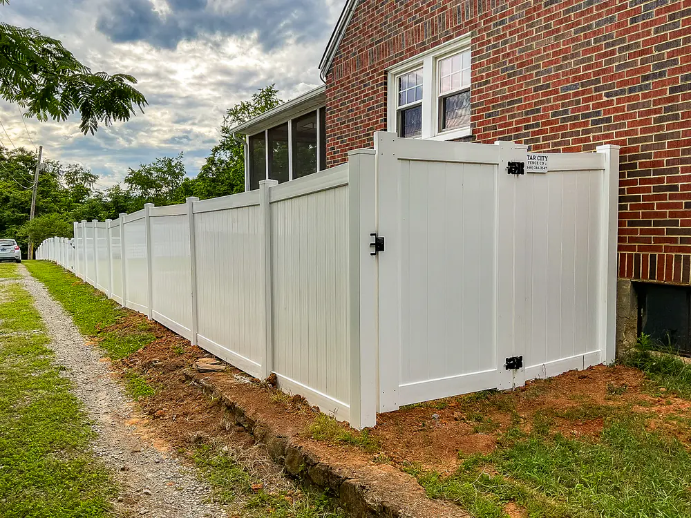 White vinyl privacy fence with gate along a gravel driveway