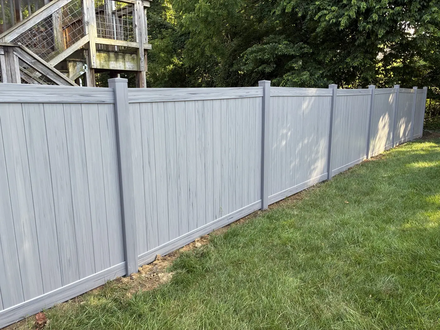 Gray wood-grain textured vinyl privacy fence in a backyard