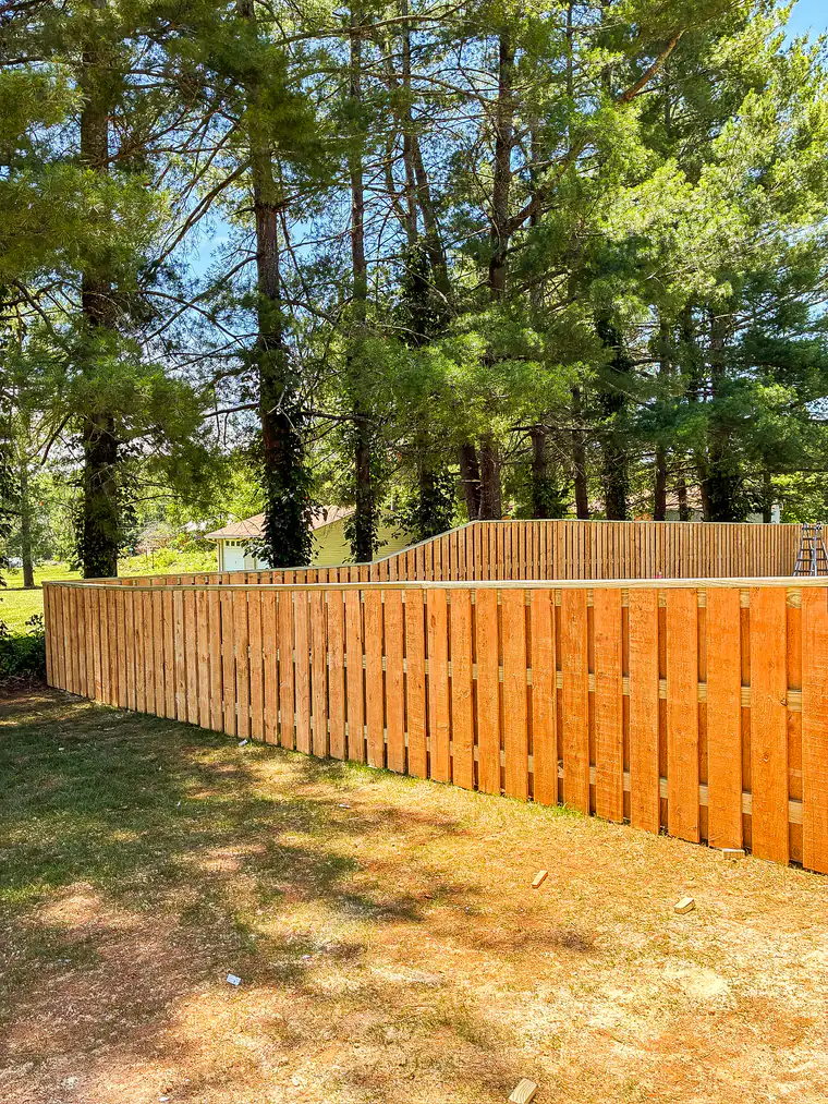 Stained shadowbox wood fence running along a treeline in Roanoke